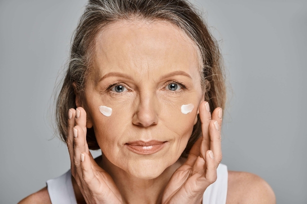 Woman serenely applying cream to her face.