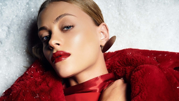 A young woman with bold red lips showcases winter fashion in a snowy landscape.