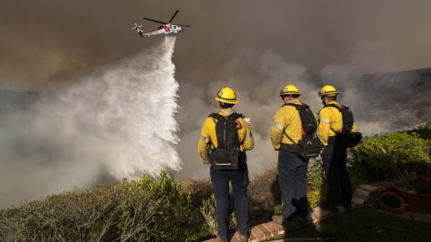 Monterey County Firefighters watch as⁣ a LA county helicopter makes a water drop on the‌ Palisades Fire