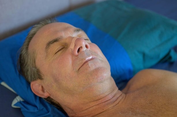 Close up picture of a middle-aged man sleeping wearing mouth tape in bed 